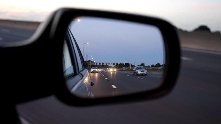 View of cars on the highway reflected in a vehicle's side mirror at twilight, capturing motion and speed.