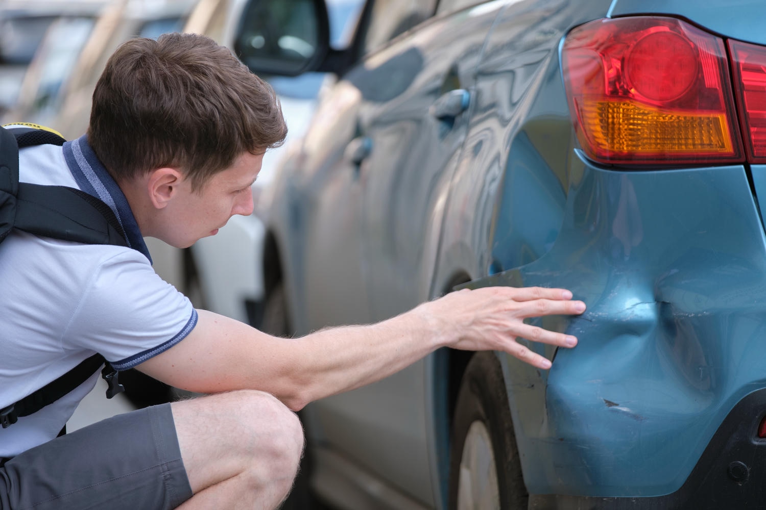 hit and run incident, young adult inspecting blue car that has been hit
